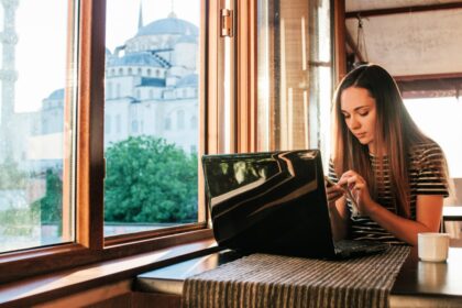 Young woman-blogger-freelancer working on a laptop in a cafe in Istanbul and calling by phone. View from the window to the world-famous Blue Mosque