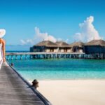 woman walks along boardwalk in stunning maldives resort with beach huts