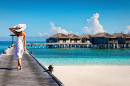 woman walks along boardwalk in stunning maldives resort with beach huts