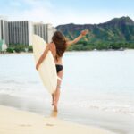 Beach fun - Happy freedom surfer woman going surfing in Waikiki beach, Honolulu city, Oahu, Hawaii, USA. Hawaiian surf girl heading for waves with surfboard living healthy active lifestyle, rear view.