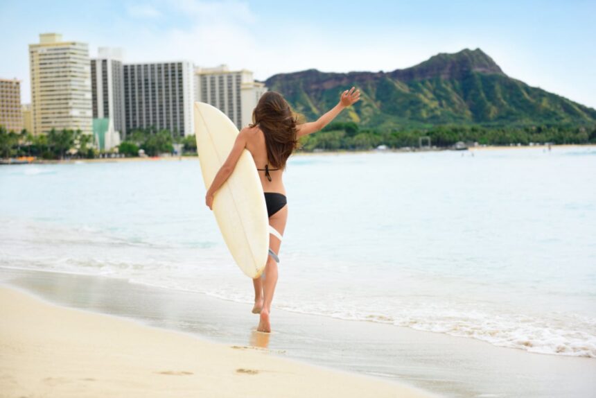 Beach fun - Happy freedom surfer woman going surfing in Waikiki beach, Honolulu city, Oahu, Hawaii, USA. Hawaiian surf girl heading for waves with surfboard living healthy active lifestyle, rear view.