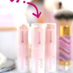 Three tubes of essence Foundation Stick standing on a vanity among brushes and mirrors. Overlaid arrow with label: $7!