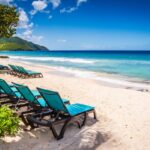 St. Croix, US Virgin Islands Two rows of teal fabric lounge chairs line white sand beach with a view of beautiful Caribbean Sea.